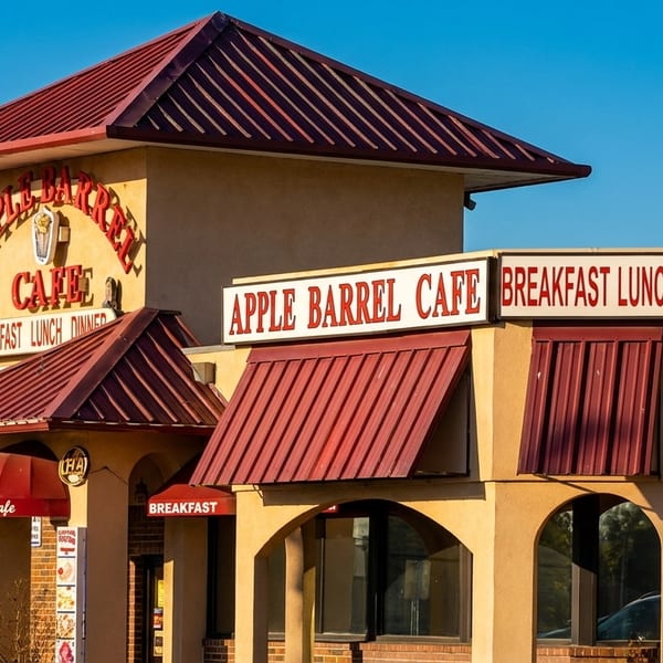 Exterior of Apple Barrel Cafe with red roofs and awnings, advertising breakfast, lunch, and dinner.