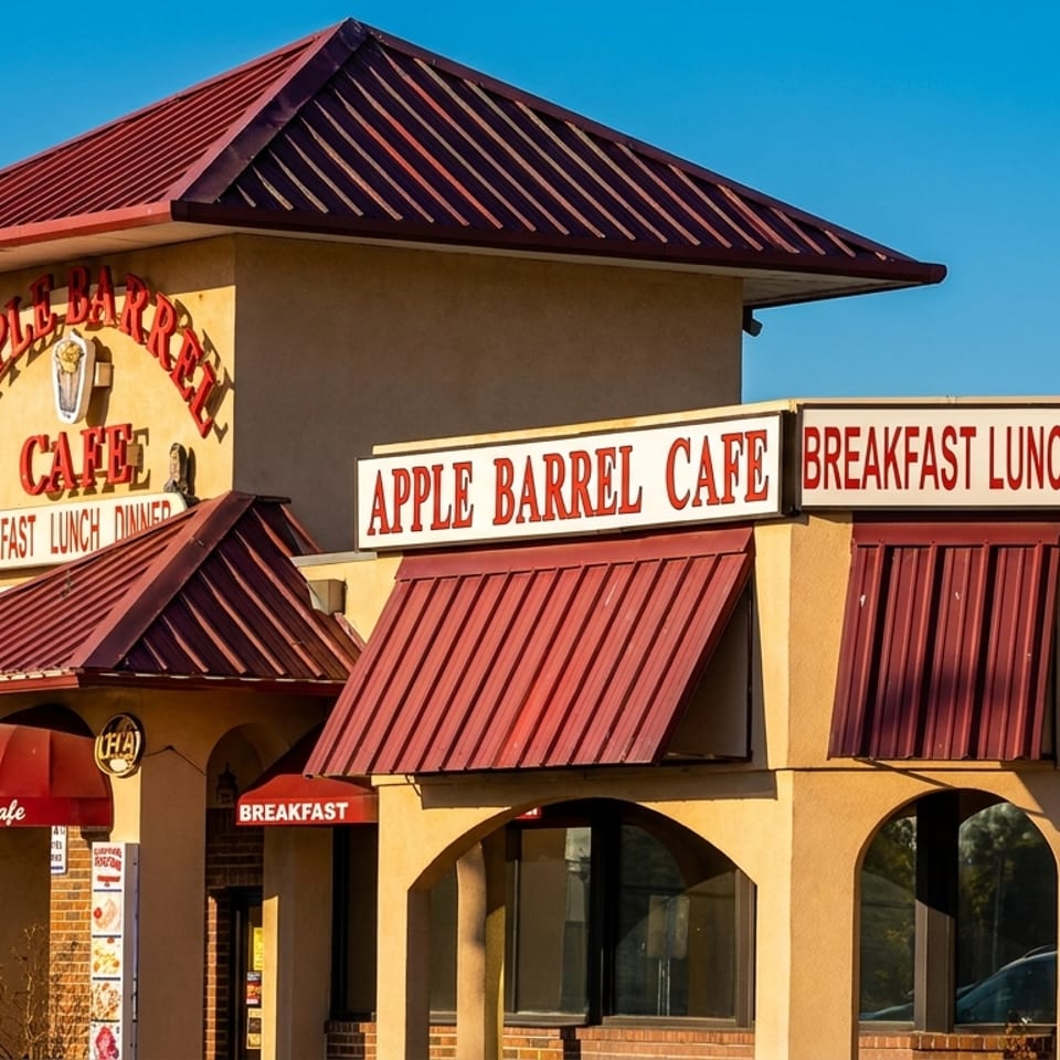 Exterior of Apple Barrel Cafe, a restaurant with red roofs and awnings, under a clear blue sky.