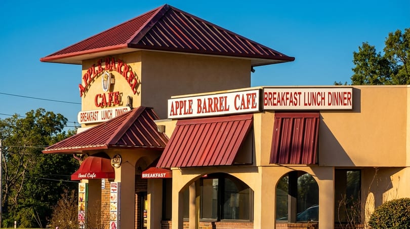 Exterior of Apple Barrel Cafe, a tan building with red roofs and signs for breakfast, lunch, dinner.