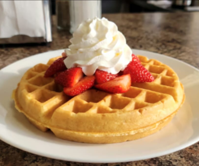 Golden waffle topped with fresh strawberries and a dollop of whipped cream on a white plate.