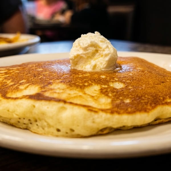 Golden-brown pancake with a dollop of melting butter on a white plate, with another plate in the background.