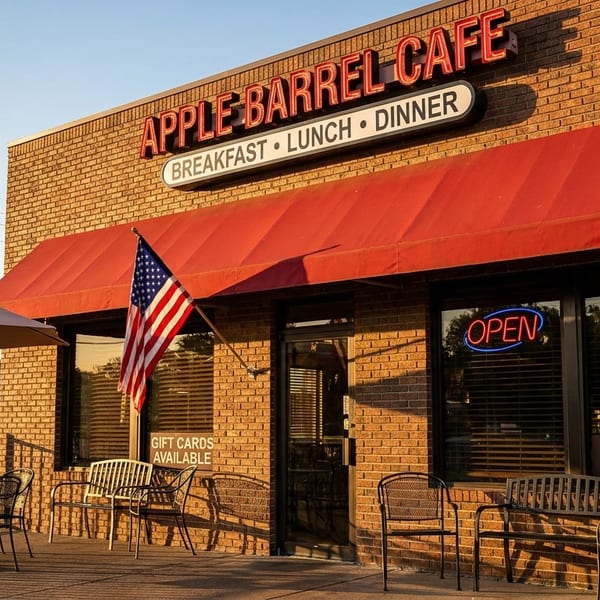 Exterior of Apple Barrel Cafe with a red awning, outdoor seating, and an American flag.
