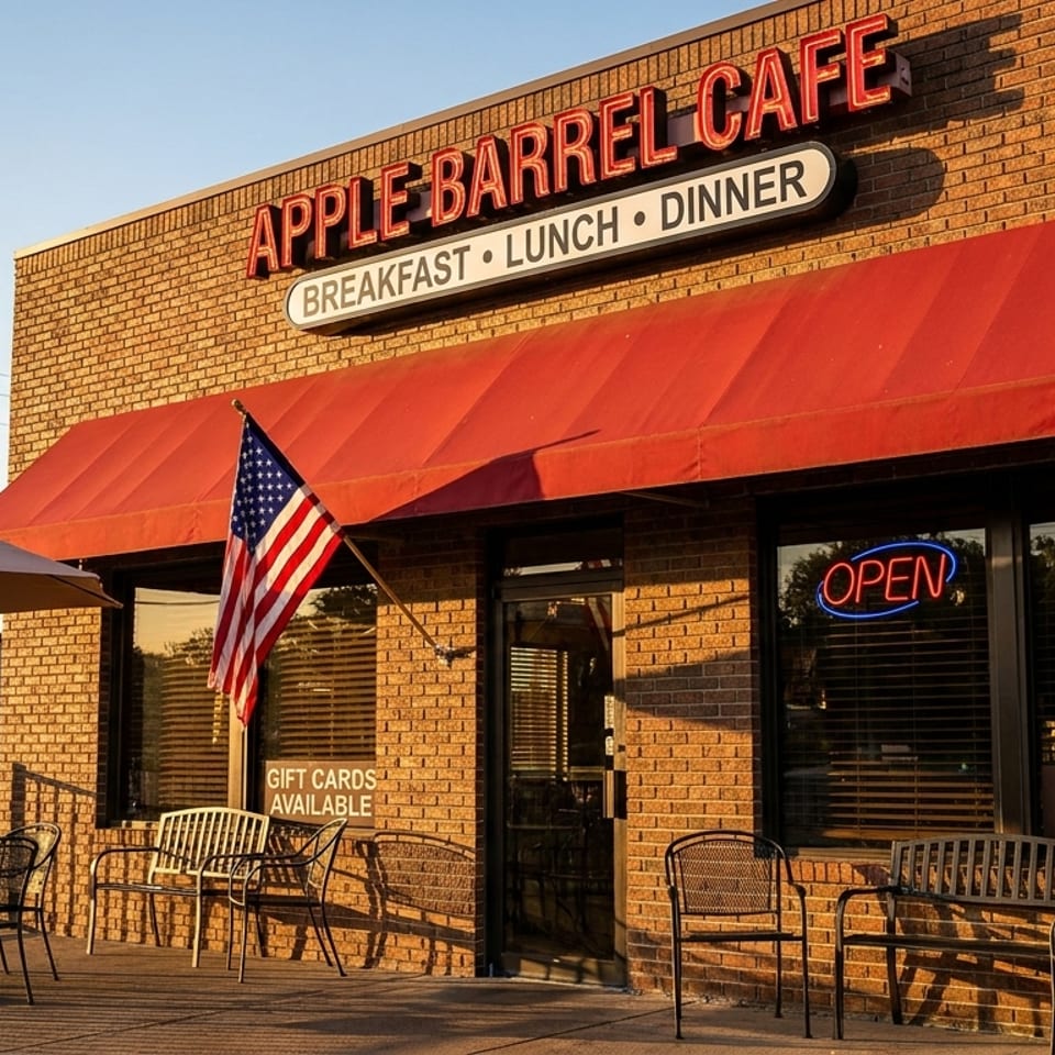 Exterior of Apple Barrel Cafe with a red awning, outdoor seating, and an American flag.