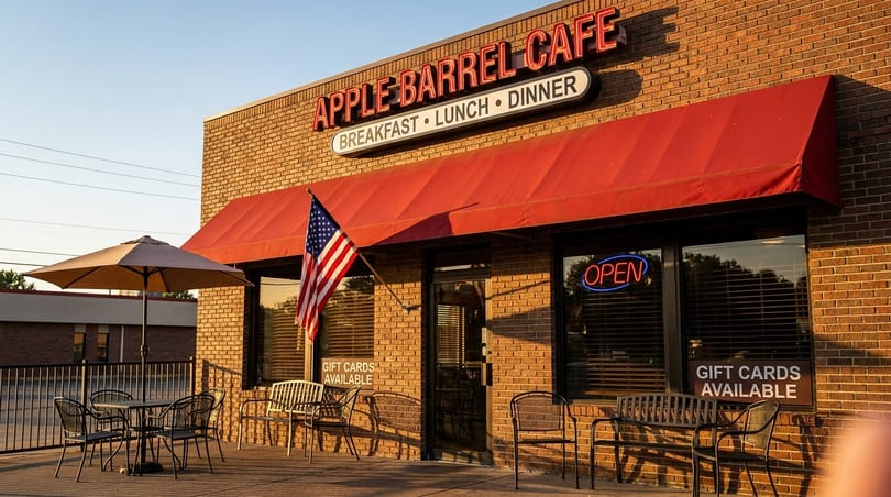 Apple Barrel Cafe's brick exterior with a red awning, American flag, and outdoor dining area.